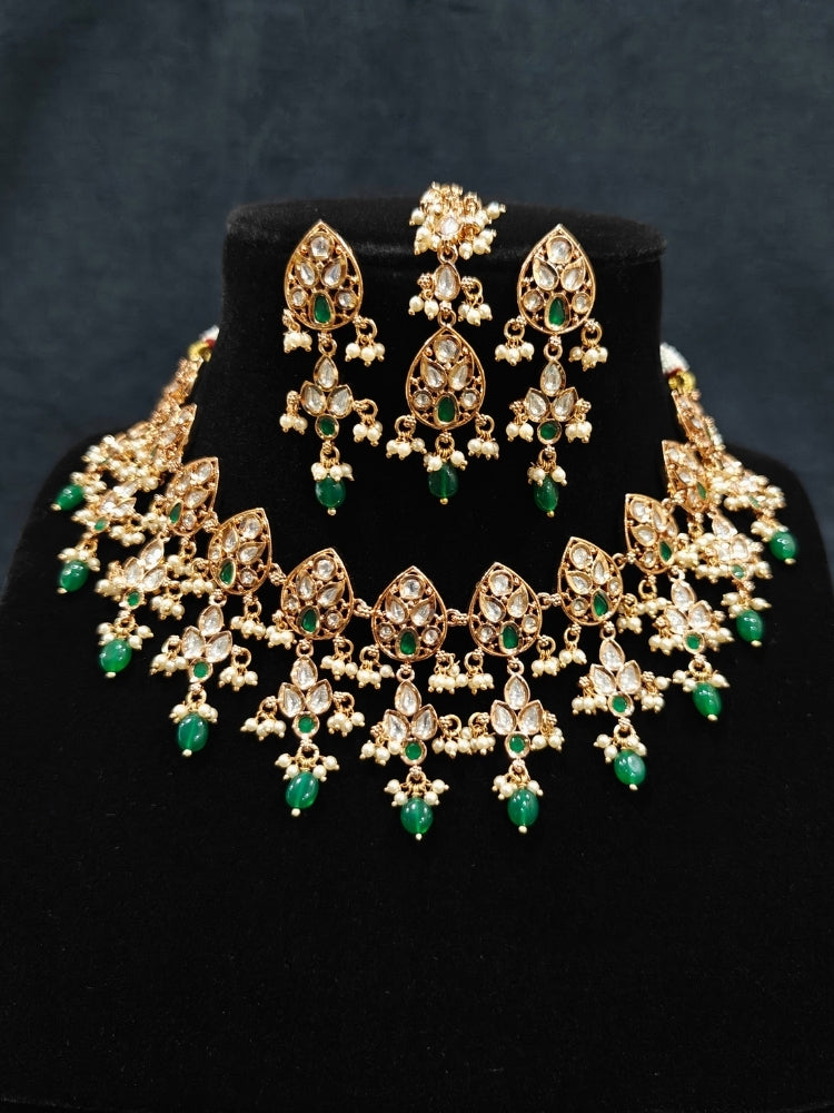 Close-up of an ornate traditional (Gold Polish) Green Collar jewellery set and earrings and maangtikka with Polki, Green Colored Stones, Tumble Beads and Pearls. Woman wearing trending Polki artificial jewelry for the wedding season in India. Woman wearing a lightweight Polki jewelry set for long wedding functions.