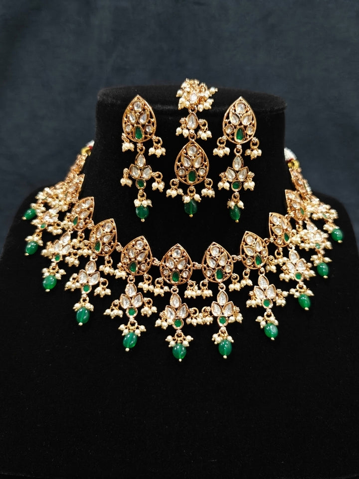 Close-up of an ornate traditional (Gold Polish) Green Collar jewellery set and earrings and maangtikka with Polki, Green Colored Stones, Tumble Beads and Pearls. Woman wearing trending Polki artificial jewelry for the wedding season in India. Woman wearing a lightweight Polki jewelry set for long wedding functions.