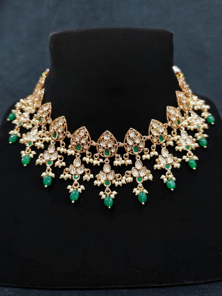 Close-up of an ornate traditional (Gold Polish) Green Collar jewellery set and earrings and maangtikka with Polki, Green Colored Stones, Tumble Beads and Pearls. Woman wearing trending Polki artificial jewelry for the wedding season in India. Woman wearing a lightweight Polki jewelry set for long wedding functions.