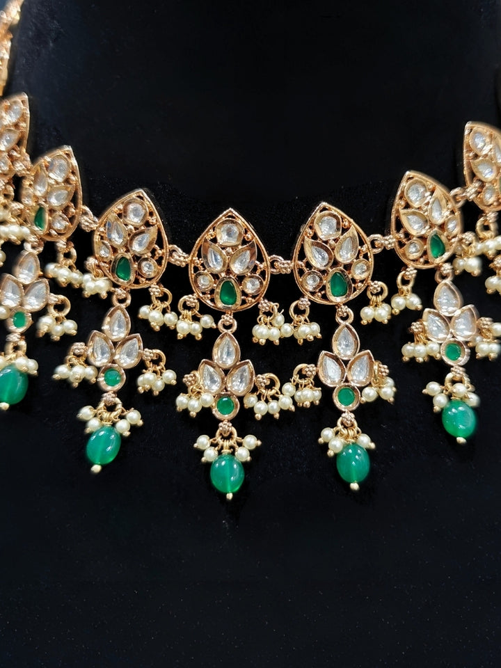 Close-up of an ornate traditional (Gold Polish) Green Collar jewellery set and earrings and maangtikka with Polki, Green Colored Stones, Tumble Beads and Pearls. Woman wearing trending Polki artificial jewelry for the wedding season in India. Woman wearing a lightweight Polki jewelry set for long wedding functions.