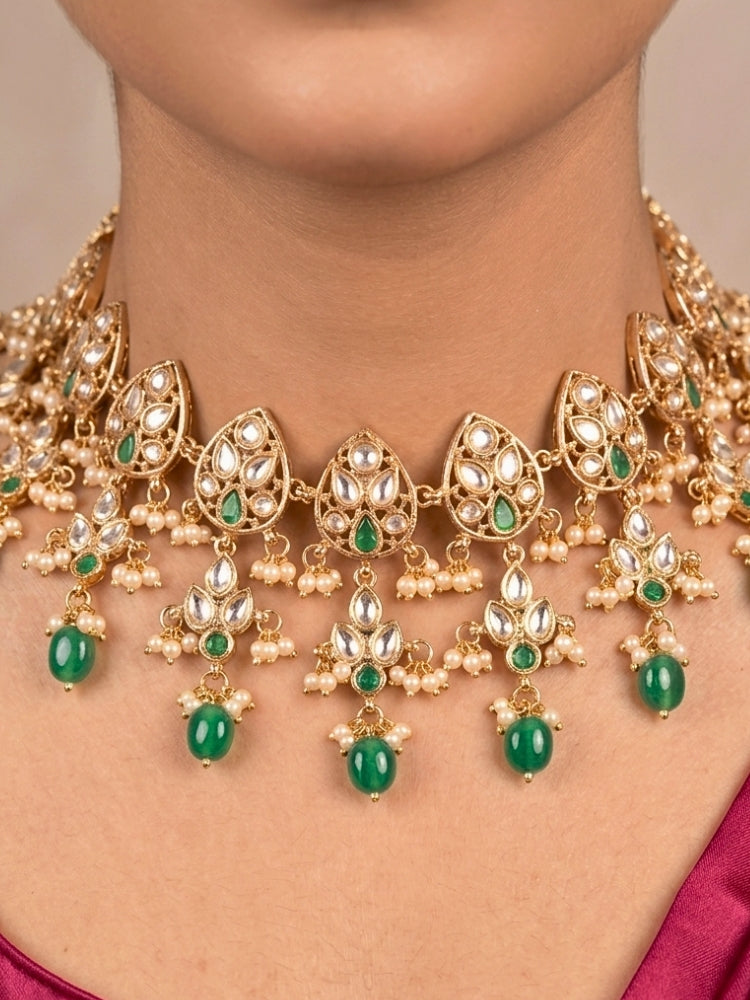 Close-up of a woman wearing an ornate traditional (Gold Polish) Green Collar jewellery set and earrings and maangtikka with Polki, Green Colored Stones, Tumble Beads and Pearls. Woman wearing trending Polki artificial jewelry for the wedding season in India. Woman wearing a lightweight Polki jewelry set for long wedding functions.