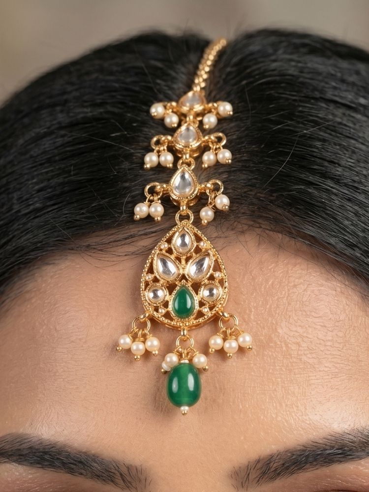 Close-up of a woman wearing an ornate traditional (Gold Polish) Green Collar jewellery set and earrings and maangtikka with Polki, Green Colored Stones, Tumble Beads and Pearls. Woman wearing trending Polki artificial jewelry for the wedding season in India. Woman wearing a lightweight Polki jewelry set for long wedding functions.