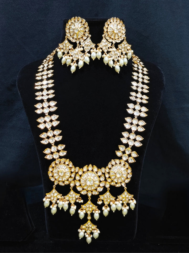 Close-up of an ornate traditional (Gold Polish) Long jewellery set and earrings with Polki and Pearls. Festive saree look completed with a Long Polki artificial jewelry set. Woman wearing trending Polki artificial jewelry for the wedding season in India.