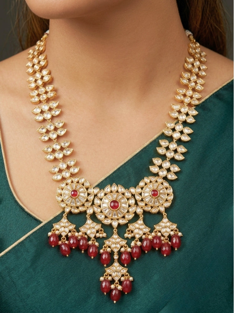 Close-up of a woman wearing an ornate traditional (Gold Polish) Ruby Red Long jewellery set and earrings with Polki, Colored Stone and Red Tumble Beads. Festive saree look completed with a Long Polki artificial jewelry set. Woman wearing trending Polki artificial jewelry for the wedding season in India.