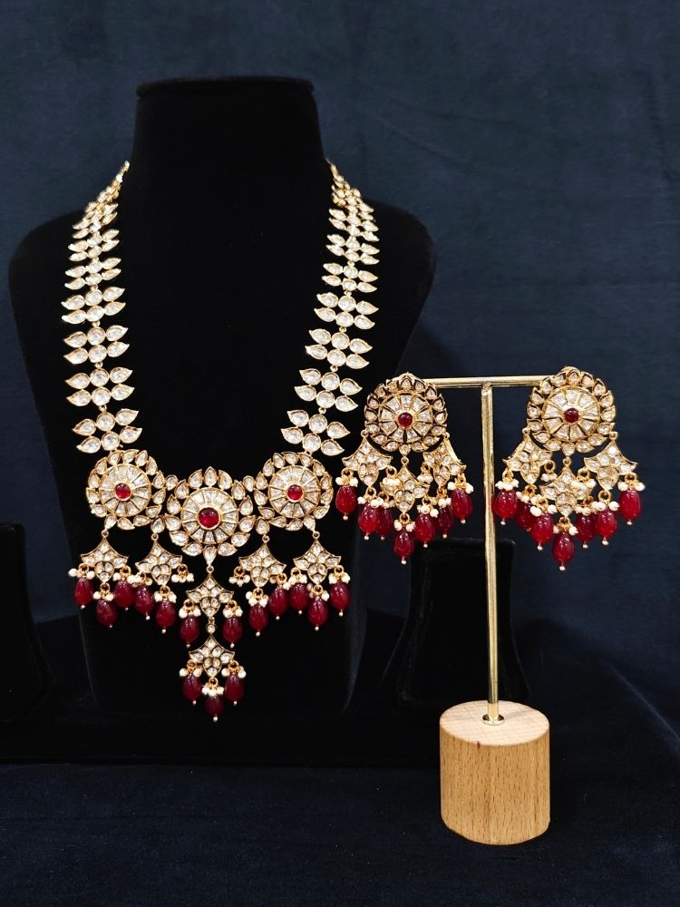 Close-up of an ornate traditional (Gold Polish) Ruby Red Long jewellery set and earrings with Polki, Colored Stone and Red Tumble Beads. Festive saree look completed with a Long Polki artificial jewelry set. Woman wearing trending Polki artificial jewelry for the wedding season in India.