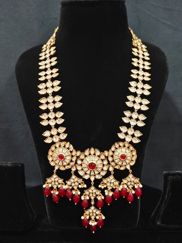 Close-up of an ornate traditional (Gold Polish) Ruby Red Long jewellery set and earrings with Polki, Colored Stone and Red Tumble Beads. Festive saree look completed with a Long Polki artificial jewelry set. Woman wearing trending Polki artificial jewelry for the wedding season in India.