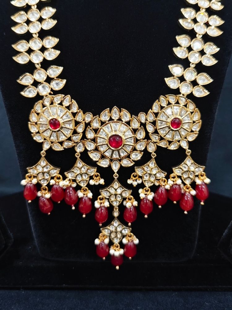 Close-up of an ornate traditional (Gold Polish) Ruby Red Long jewellery set and earrings with Polki, Colored Stone and Red Tumble Beads. Festive saree look completed with a Long Polki artificial jewelry set. Woman wearing trending Polki artificial jewelry for the wedding season in India.