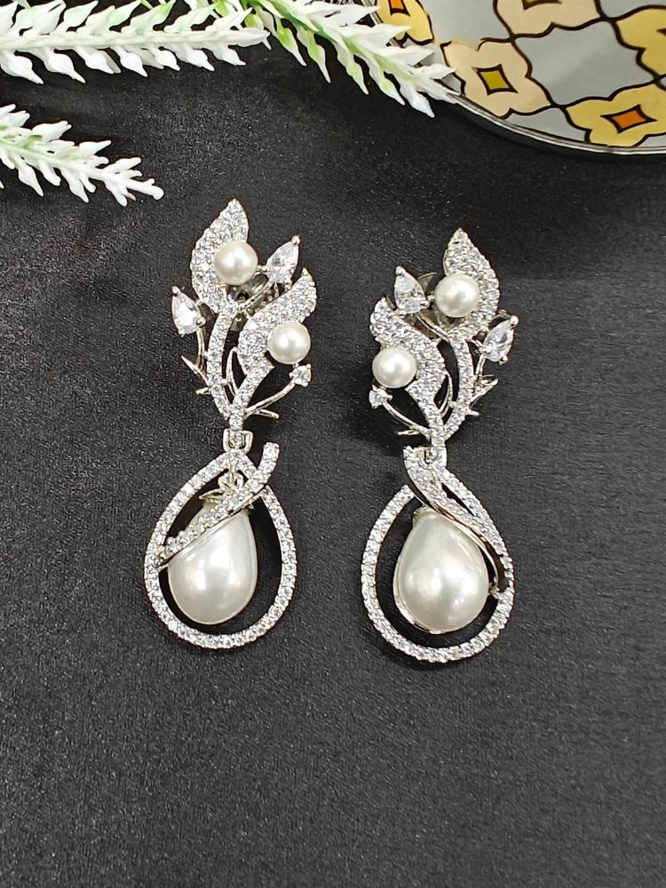 The Laurie Earrings, featuring ornate white leaf-shaped designs, pearl accents, and sparkling stones, capture the charm of western fashion as they rest on a black surface with decorative white foliage. Pearl Earrings, Date night jewellery. 