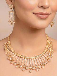 The Lavanya Necklace Set features a gold Champaign necklace with vertical bars topped by teardrop-shaped champagne colored American Diamonds, paired with matching dangling earrings and displayed on a blue velvet bust with ornate embroidery on the left.