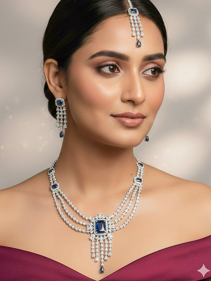 "A close-up shot of a bride wearing a stunning artificial diamond necklace with navy blue colored stone and matching earrings with maangtikka, designed to complement bridal attire. This affordable diamond necklace set is perfect for brides seeking luxurious but cost-effective wedding jewelry in India."
