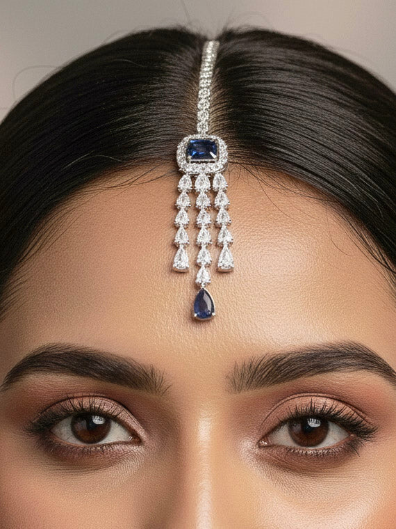 "A woman in a traditional saree, wearing a gorgeous artificial diamond necklace with navy blue colored stone paired with diamond earrings and diamond maangtikka. This artificial diamond jewelry set offers a traditional yet modern touch for Indian brides, designed to add elegance and sophistication to any occasion."
