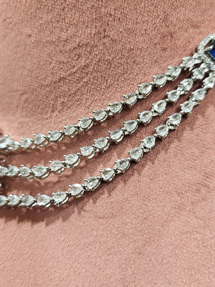 Close-up of an ornate Indo-western Navy Blue Diamond Silver Collar jewellery set and earrings and maangtikka with American Diamond & Colored Stones. Close-up shot of a high-quality American diamond artificial necklace worn for festive celebrations. A sparkling American diamond necklace for reception night.
