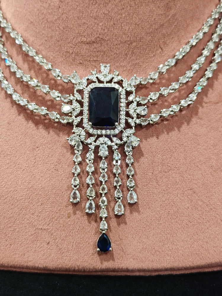 Close-up of an ornate Indo-western Navy Blue Diamond Silver Collar jewellery set and earrings and maangtikka with American Diamond & Colored Stones. Close-up shot of a high-quality American diamond artificial necklace worn for festive celebrations. A sparkling American diamond necklace for reception night.