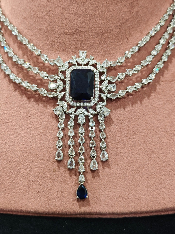 Close-up of an ornate Indo-western Navy Blue Diamond Silver Collar jewellery set and earrings and maangtikka with American Diamond & Colored Stones. Close-up shot of a high-quality American diamond artificial necklace worn for festive celebrations. A sparkling American diamond necklace for reception night.