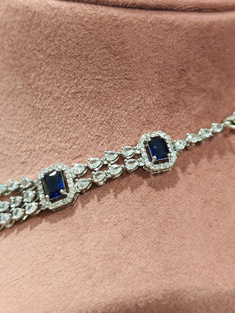 Close-up of an ornate Indo-western Navy Blue Diamond Silver Collar jewellery set and earrings and maangtikka with American Diamond & Colored Stones. Close-up shot of a high-quality American diamond artificial necklace worn for festive celebrations. A sparkling American diamond necklace for reception night.
