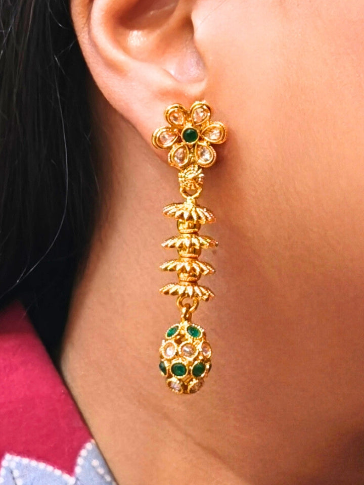 A close-up of a womans ear wearing Laxmi Green Earrings featuring a floral design with dangling gold elements and green gemstone accents at the oval drop at the bottom —ideal for wedding ceremony jewelry.