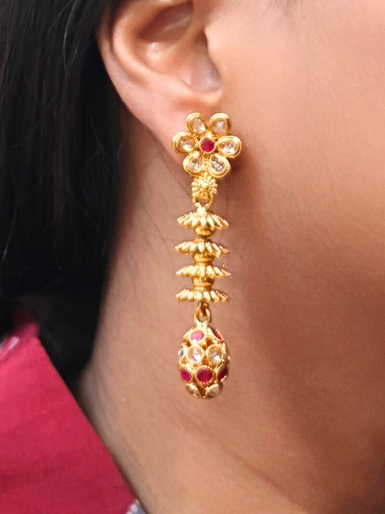 A close-up of a womans ear wearing Laxmi Red Earrings featuring a floral design with dangling gold elements and Red gemstone accents at the oval drop at the bottom —ideal for wedding ceremony jewelry.