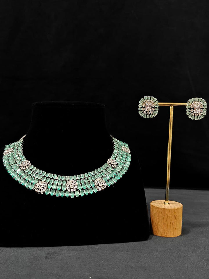 "An exquisite artificial diamond necklace with mint green colored stone and matching earrings, designed for the perfect engagement look. This stunning artificial diamond jewelry set offers luxury and sophistication while being an affordable alternative to natural diamonds." Reception-ready look featuring a statement American diamond jewelry set.