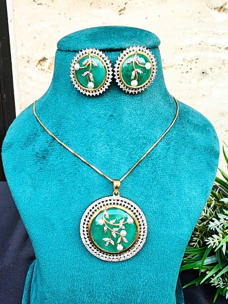 The Lisa Mint Green Pendant Set features a gold necklace and earrings with round Green stones, white floral designs, pearl accents, and a bold Green pendant—beautifully displayed on a teal stand and perfect for your cocktail gown.