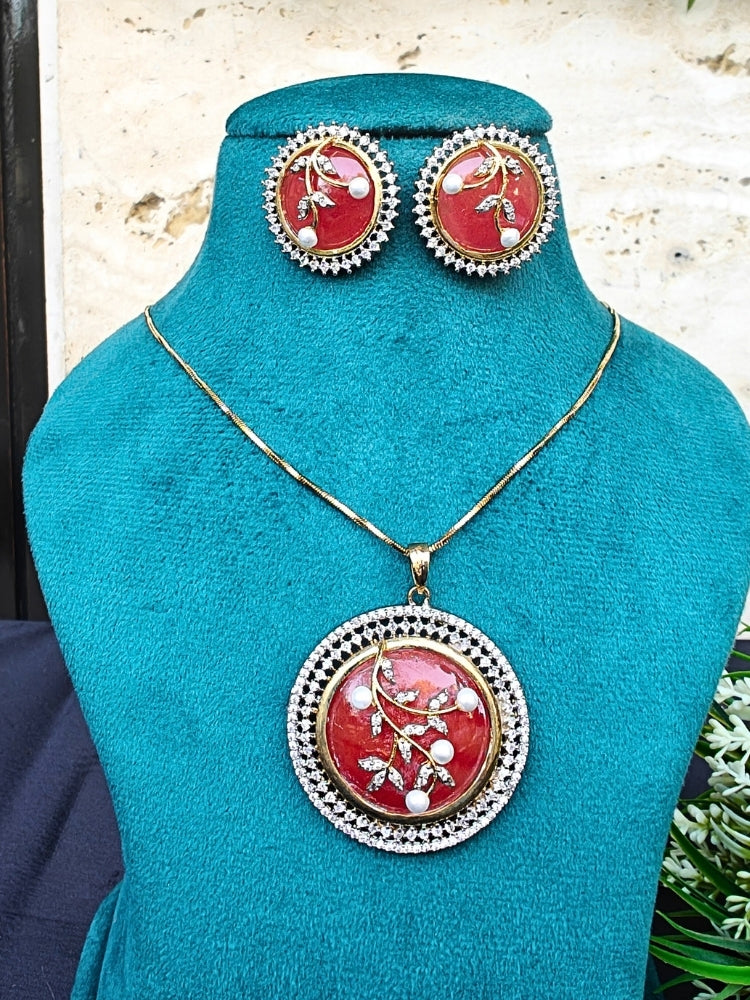 The Lisa Orange Pendant Set, displayed on a teal stand, features a gold necklace and matching earrings with round orange pendants, accented by pearl and crystal floral designs bordered by American Diamonds—ideal for cocktail gowns.