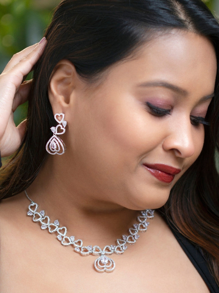 The Love Necklace Set features a heart-shaped white necklace and matching earrings with sparkling American Diamonds, elegantly presented in a black velvet box—perfect to complement your favorite cocktail gown.