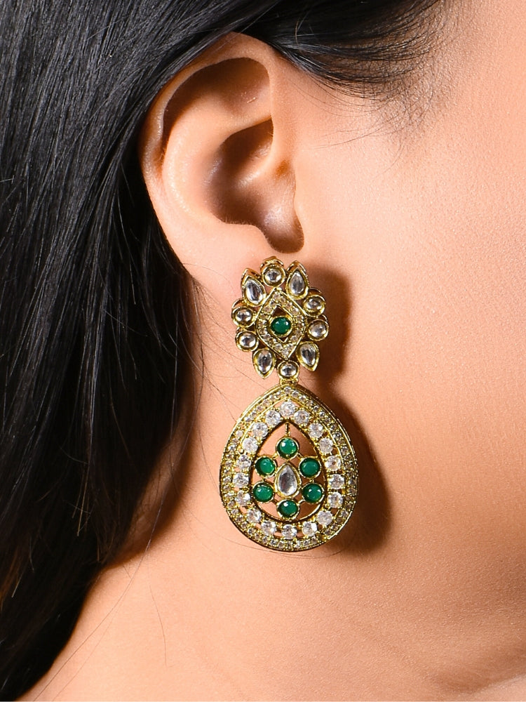 A woman with long dark hair wears a black top and the Lupin Dark Green Necklace Set, featuring ornate ethnic jewelry with emerald green accents and matching earrings. The hasli necklace set is made in mehendi polish, along with emerald green stones and american diamonds. 