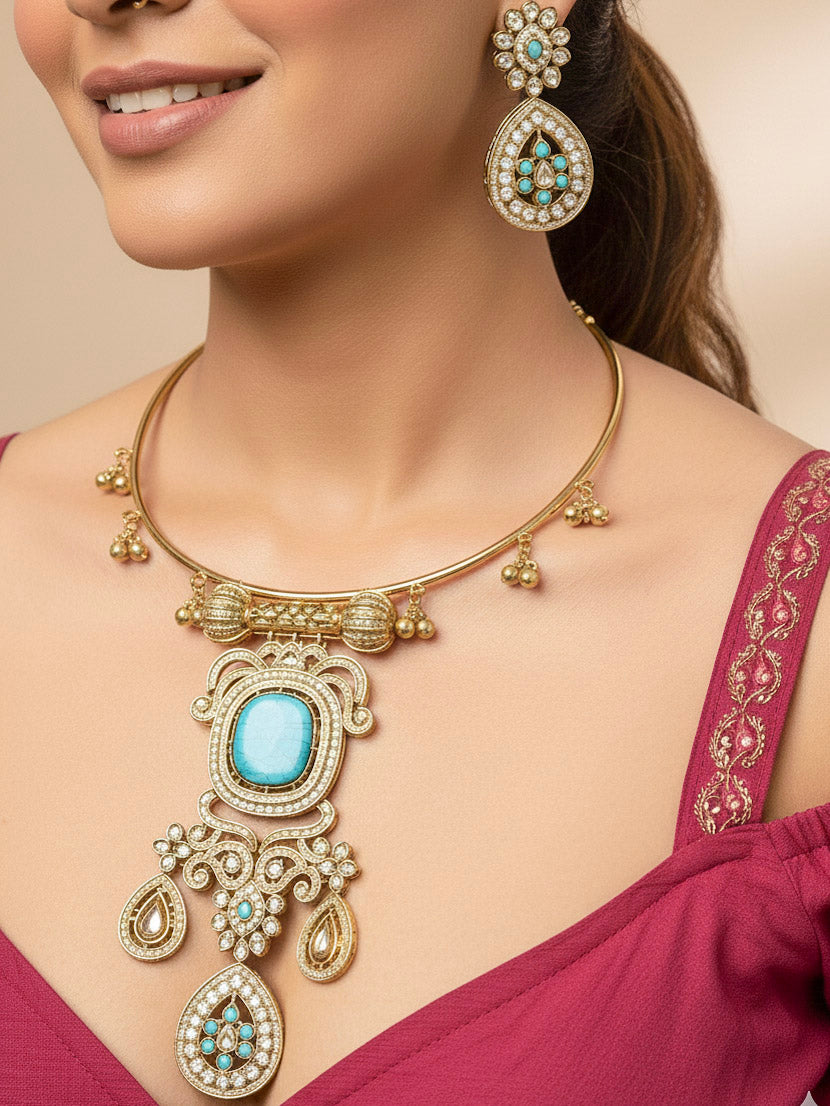 Discover the elegance of the Lupin Hasli Necklace Set, featuring a radiant Mint Blue Monalisa stone, sparkling American diamonds, and charming tiny ghungroos. Perfect for saris, weddings, and festive occasions. Put on a blue mannequin, and a beige embroidered fabric draped over the shoulder