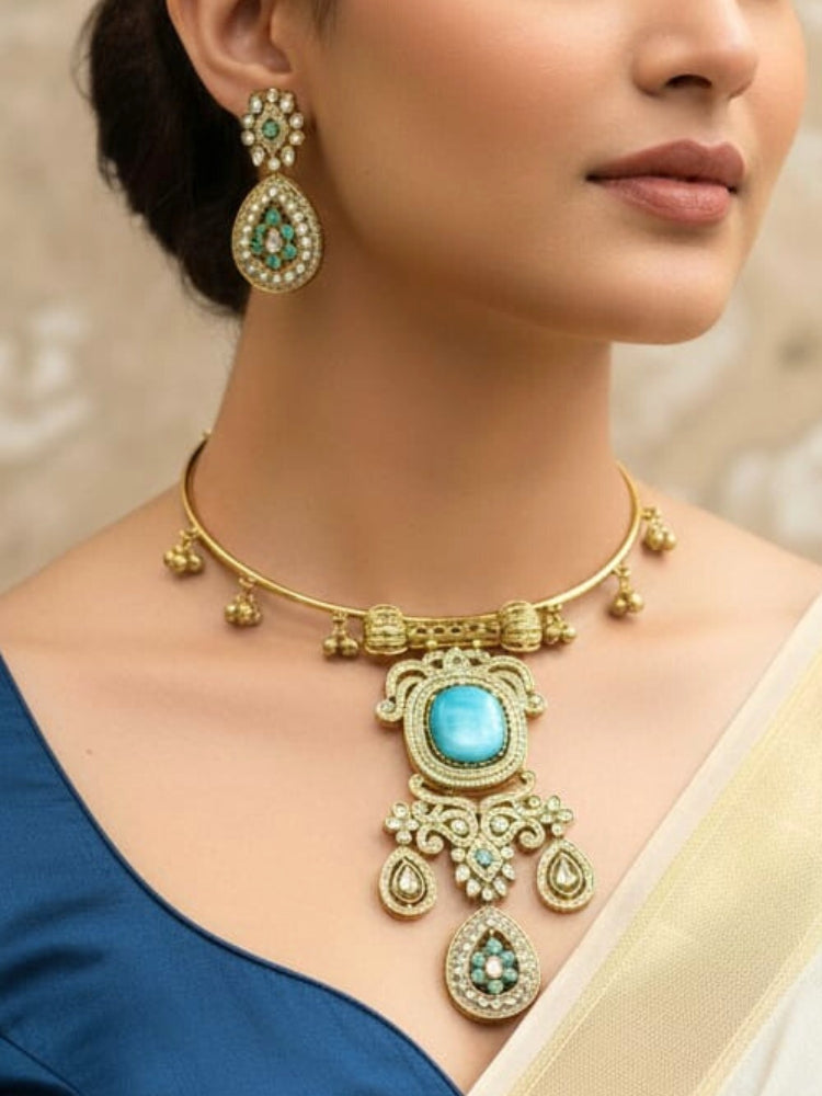 Discover the elegance of the Lupin Hasli Necklace Set, featuring a radiant Mint Blue Monalisa stone, sparkling American diamonds, and charming tiny ghungroos. Perfect for saris, weddings, and festive occasions. Put on a blue mannequin, and a beige embroidered fabric draped over the shoulder