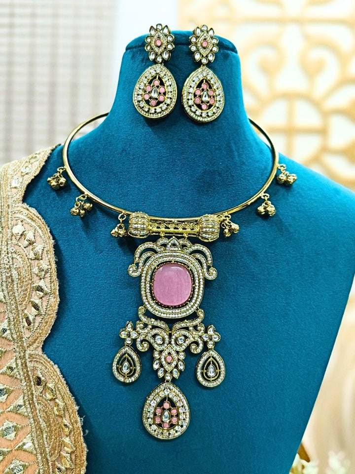 Discover the elegance of the Lupin Hasli Necklace Set, featuring a radiant Mint Pink Monalisa stone, sparkling American diamonds, and charming tiny ghungroos. Perfect for saris, weddings, and festive occasions. Put on a blue mannequin, and a beige embroidered fabric draped over the shoulder