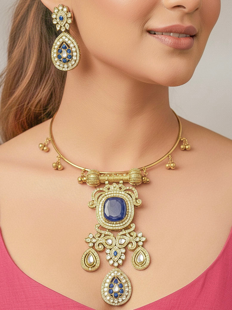 Discover the elegance of the Lupin Hasli Necklace Set, featuring a radiant Navy Blue Monalisa stone, sparkling American diamonds, and charming tiny ghungroos. Perfect for saris, weddings, and festive occasions. Put on a white mannequin, and a beige embroidered fabric draped over the shoulder