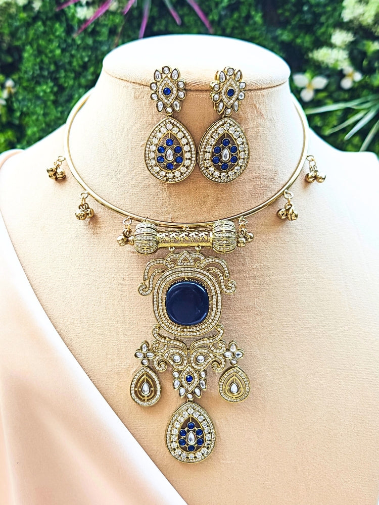 Discover the elegance of the Lupin Hasli Necklace Set, featuring a radiant Navy Blue Monalisa stone, sparkling American diamonds, and charming tiny ghungroos. Perfect for saris, weddings, and festive occasions. Put on a white mannequin, and a beige embroidered fabric draped over the shoulder