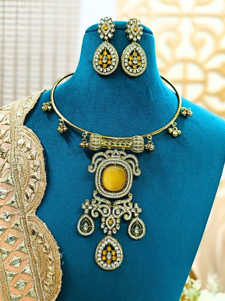 Discover the elegance of the Lupin Hasli Necklace Set, featuring a radiant Yellow Monalisa stone, sparkling American diamonds, and charming tiny ghungroos. Perfect for saris, weddings, and festive occasions. Put on a blue mannequin, and a beige embroidered fabric draped over the shoulder