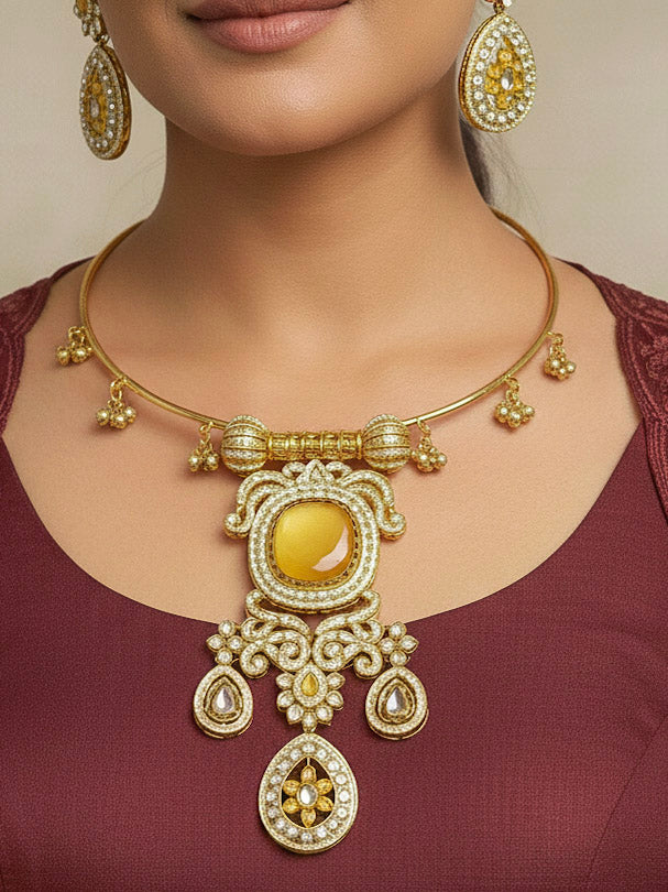 Discover the elegance of the Lupin Hasli Necklace Set, featuring a radiant Yellow Monalisa stone, sparkling American diamonds, and charming tiny ghungroos. Perfect for saris, weddings, and festive occasions. Put on a blue mannequin, and a beige embroidered fabric draped over the shoulder