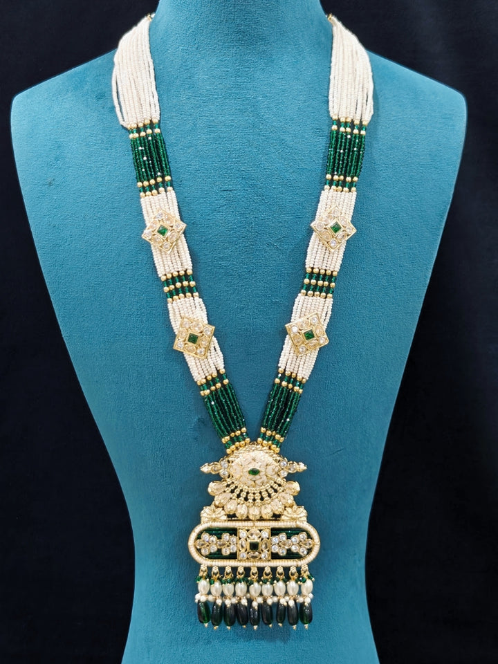 Close-up of an ornate traditional Green Rajwadi gold Long jewellery set and earrings  with  Pearls, Tumble Beads, Meenakari, Moissanite Kundan, Bandhai Work and Hydro Crystals. Close-up of detailed Rajwadi craftsmanship in artificial jewelry. Festive look completed with a luxury Rajwadi imitation necklace.