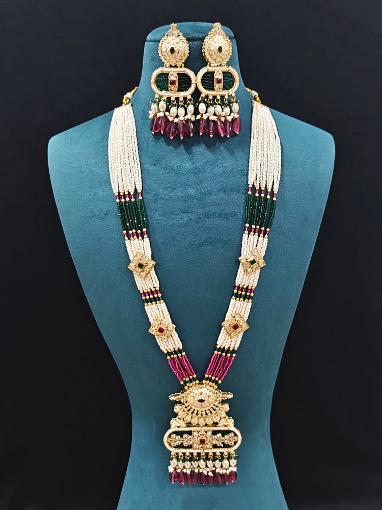 Close-up of an ornate traditional Ruby Pink and Green Rajwadi gold Long jewellery set and earrings  with  Pearls, Tumble Beads, Meenakari, Moissanite Kundan, Bandhai Work and Hydro Crystals. Woman wearing a Rajwadi necklace for a reception function. Wedding guest styling a Rajwadi artificial necklace with a Anarkali.