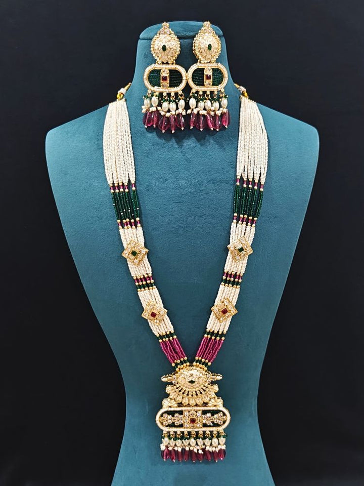 Close-up of an ornate traditional Ruby Pink and Green Rajwadi gold Long jewellery set and earrings  with  Pearls, Tumble Beads, Meenakari, Moissanite Kundan, Bandhai Work and Hydro Crystals. Woman wearing a Rajwadi necklace for a reception function. Wedding guest styling a Rajwadi artificial necklace with a Anarkali.