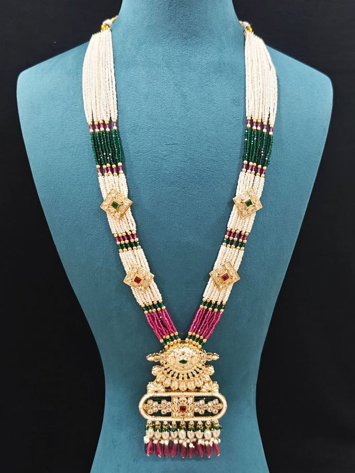 Close-up of an ornate traditional Ruby Pink and Green Rajwadi gold Long jewellery set and earrings  with  Pearls, Tumble Beads, Meenakari, Moissanite Kundan, Bandhai Work and Hydro Crystals. Woman wearing a Rajwadi necklace for a reception function. Wedding guest styling a Rajwadi artificial necklace with a Anarkali.