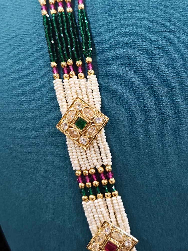 Close-up of an ornate traditional Ruby Pink and Green Rajwadi gold Long jewellery set and earrings  with  Pearls, Tumble Beads, Meenakari, Moissanite Kundan, Bandhai Work and Hydro Crystals. Woman wearing a Rajwadi necklace for a reception function. Wedding guest styling a Rajwadi artificial necklace with a Anarkali.