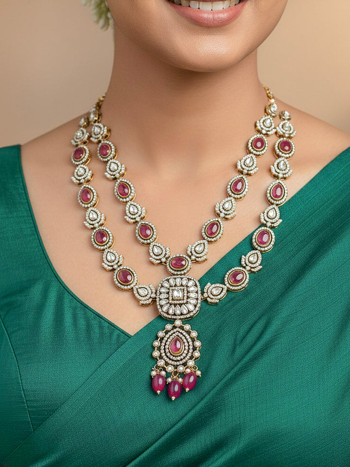 Close-up of a woman wearing an ornate traditional Magenta Diamond Collar Layered jewellery set and earrings and maangtikka with Kundan, American Diamonds, Tumble stones, Black Polish and Colored Stones. A woman wearing a luxury American diamond necklace set styled beautifully for a wedding guest look in India. Close-up of a bridal look featuring an anti-tarnish American diamond artificial necklace.