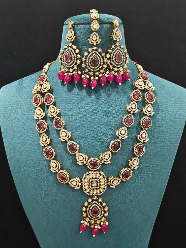 Close-up of an ornate traditional Magenta Diamond Collar Layered jewellery set and earrings and maangtikka with Kundan, American Diamonds, Tumble stones, Black Polish and Colored Stones. A luxury American diamond necklace set styled beautifully for a wedding guest look in India. Close-up of a bridal look featuring an anti-tarnish American diamond artificial necklace.