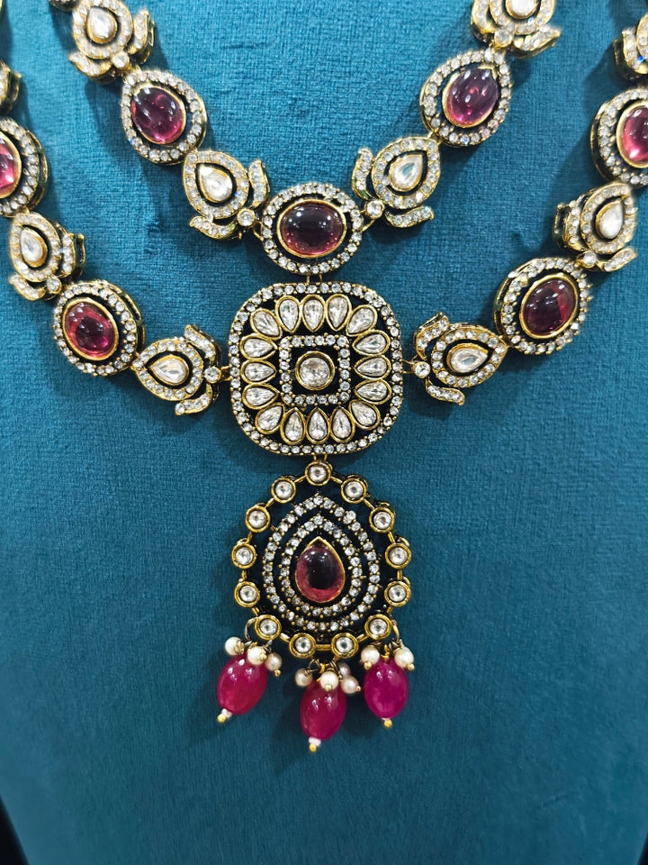 Close-up of an ornate traditional Magenta Diamond Collar Layered jewellery set and earrings and maangtikka with Kundan, American Diamonds, Tumble stones, Black Polish and Colored Stones. A luxury American diamond necklace set styled beautifully for a wedding guest look in India. Close-up of a bridal look featuring an anti-tarnish American diamond artificial necklace.