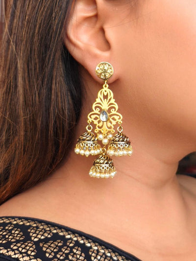 A close-up of a womans ear adorned with Mahika Earrings— Long earrings featuring filigree design with a kundan stone in the middle. It has 3 dangling jhumkins with pearls hanging at the bottom. Her straight brown hair and black outfit highlight the stunning ethnic jewelry.
