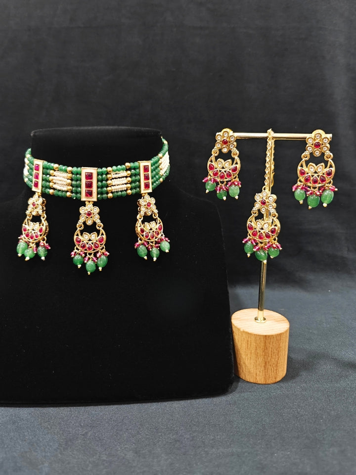 Close-up of an ornate traditional (Gold Polish) Green and Pink  Choker jewellery set and earrings and maangtikka with Pearls, Beads, Pink Colored Stones, Bandhai Work, Tumble Beads. Mehendi ceremony look completed with a handcrafted Colored Stone jewelry set. Woman styling a vibrant Colored Stone necklace with a festive saree.