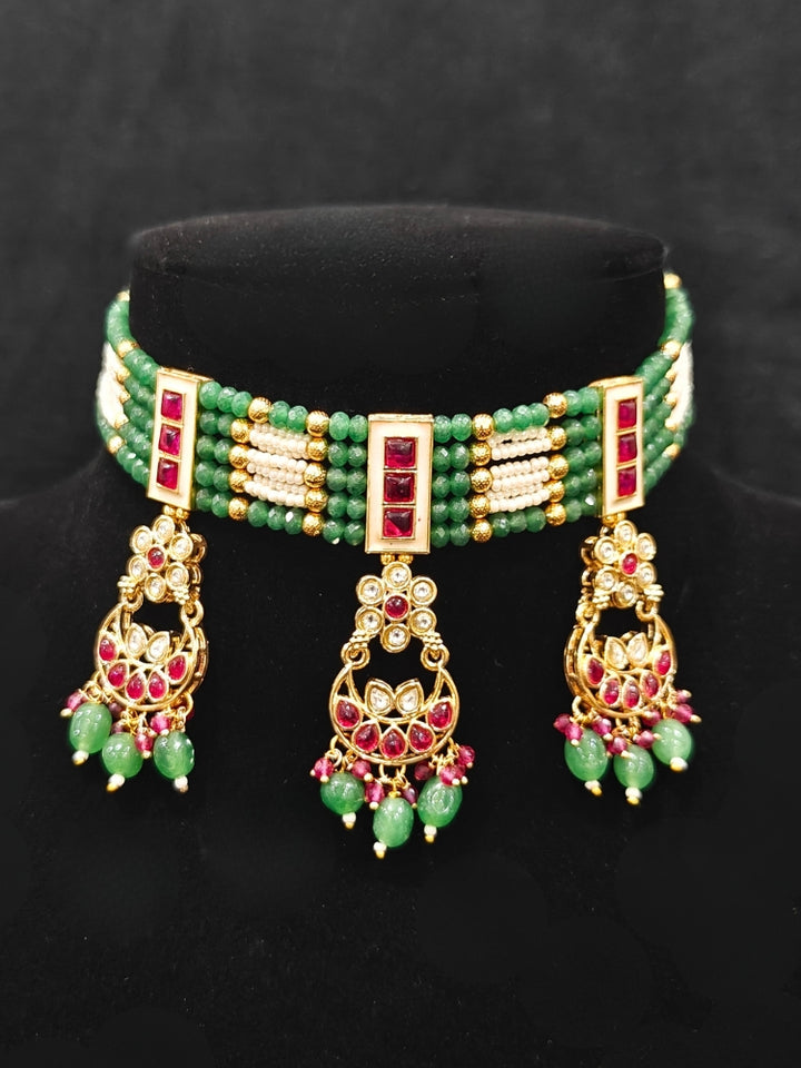 Close-up of an ornate traditional (Gold Polish) Green and Pink  Choker jewellery set and earrings and maangtikka with Pearls, Beads, Pink Colored Stones, Bandhai Work, Tumble Beads. Mehendi ceremony look completed with a handcrafted Colored Stone jewelry set. Woman styling a vibrant Colored Stone necklace with a festive saree.