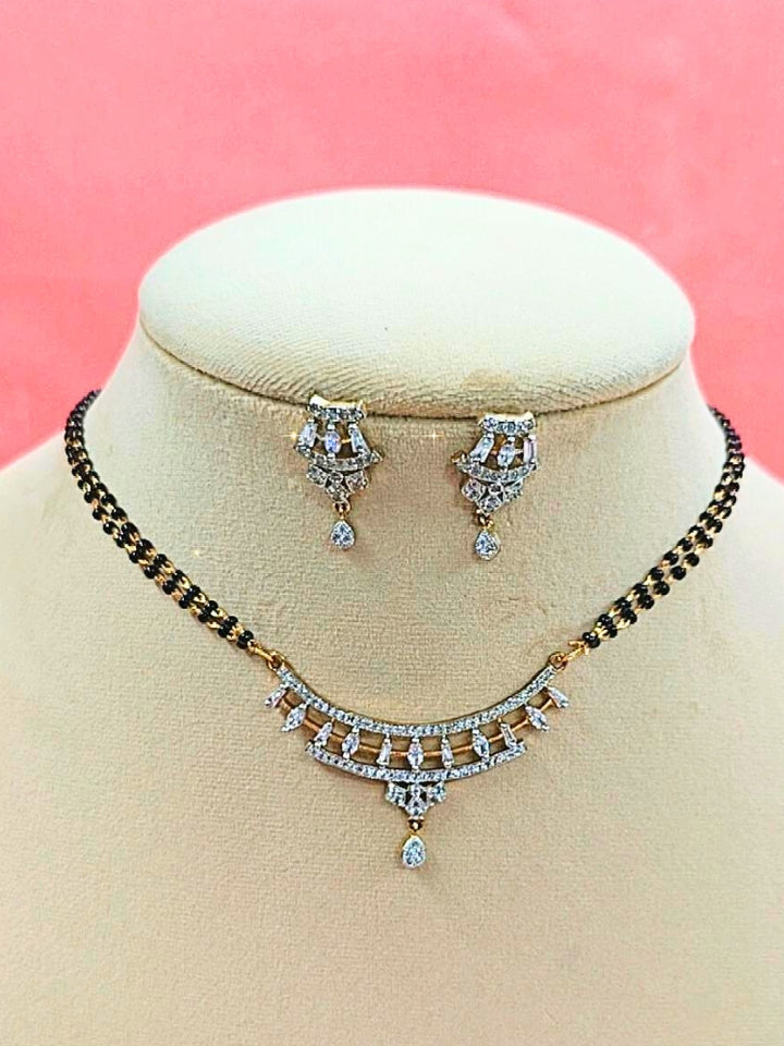 Mahira Mangalsutra—a gold necklace with black mangalsutra beads and matching earrings, pendant featuring sparkling American Diamonds—set against a cream dummy, perfect for your wedding ceremony dress. Diamond mangalsutra. Modern mangalsutra. 