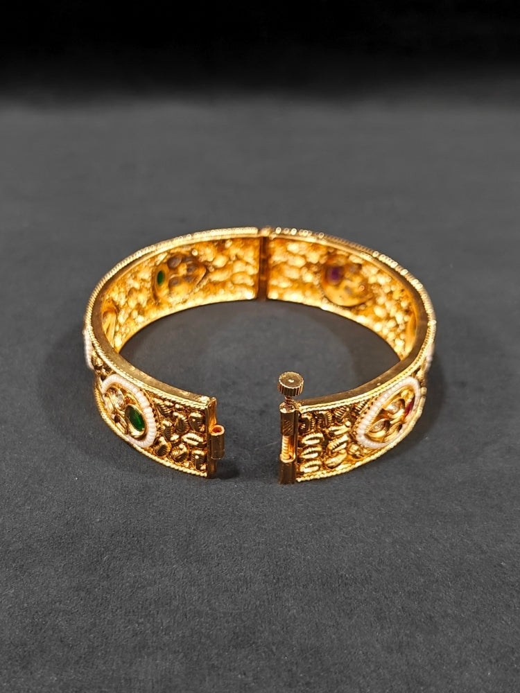 Close-up of an ornate traditional Rajwadi gold Bangle with Bandhai Work, Red & Green Colored Stone and Pearls. Festive celebration look enhanced with statement artificial  Rajwadi bangles. Luxury artificial Rajwadi bangles styled for a wedding function.