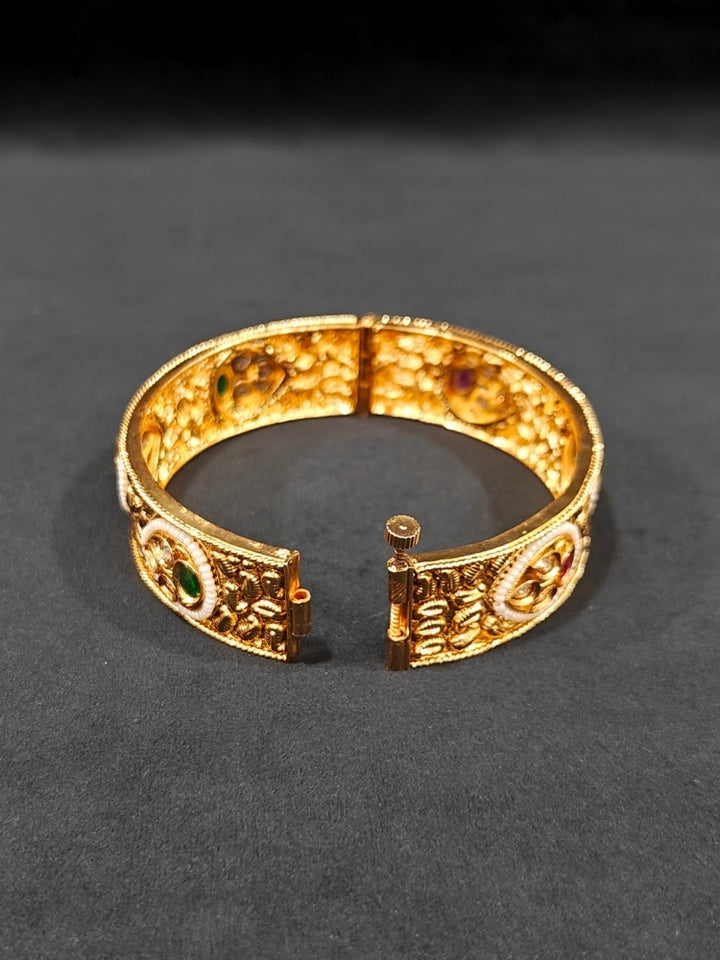 Close-up of an ornate traditional Rajwadi gold Bangle with Bandhai Work, Red & Green Colored Stone and Pearls. Festive celebration look enhanced with statement artificial  Rajwadi bangles. Luxury artificial Rajwadi bangles styled for a wedding function.