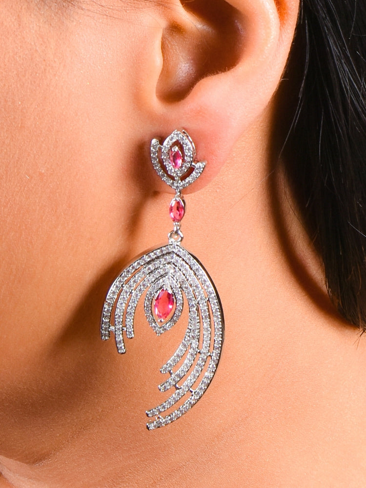 A close-up of a womans ear wearing the Marcelline Red Earrings—large, elegant silver earrings with sparkling American Diamonds, pink gemstones, and a layered fan-like design that dangles below the earlobe.