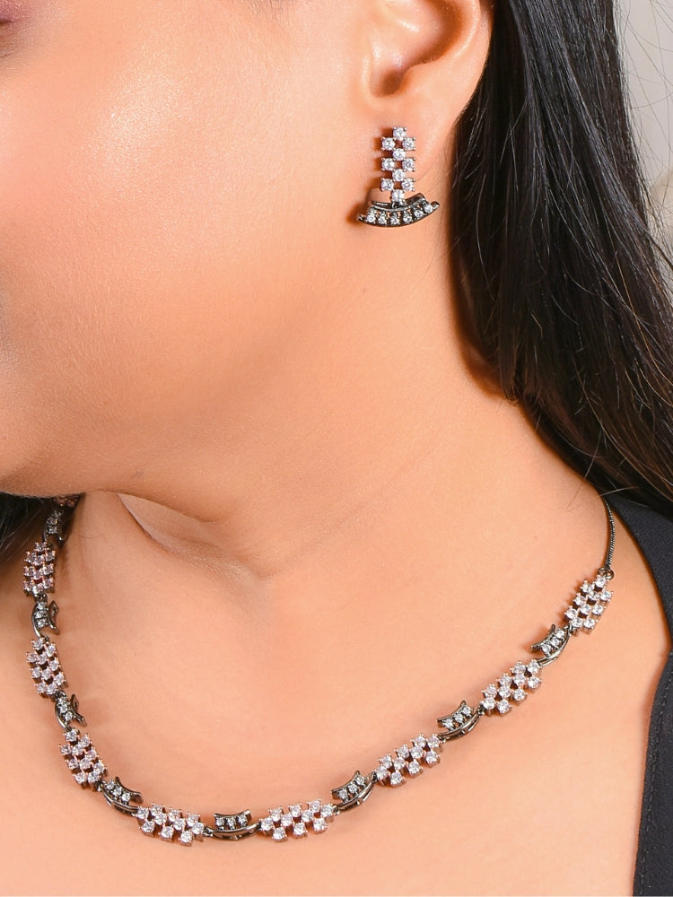 A woman showcases the Margaret Necklace Set, a matching American Diamonds jewelry set with a black polish necklace and earrings adorned with clusters of American diamonds and colored stones, elegantly set against her skin and dark hair.