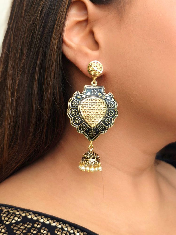 A close-up of a womans ear wearing the Margot Earrings—large black earrings with ornate filigree work and a small pearl-adorned jhumka. Her straight brown hair frames the detailed design beautifully.